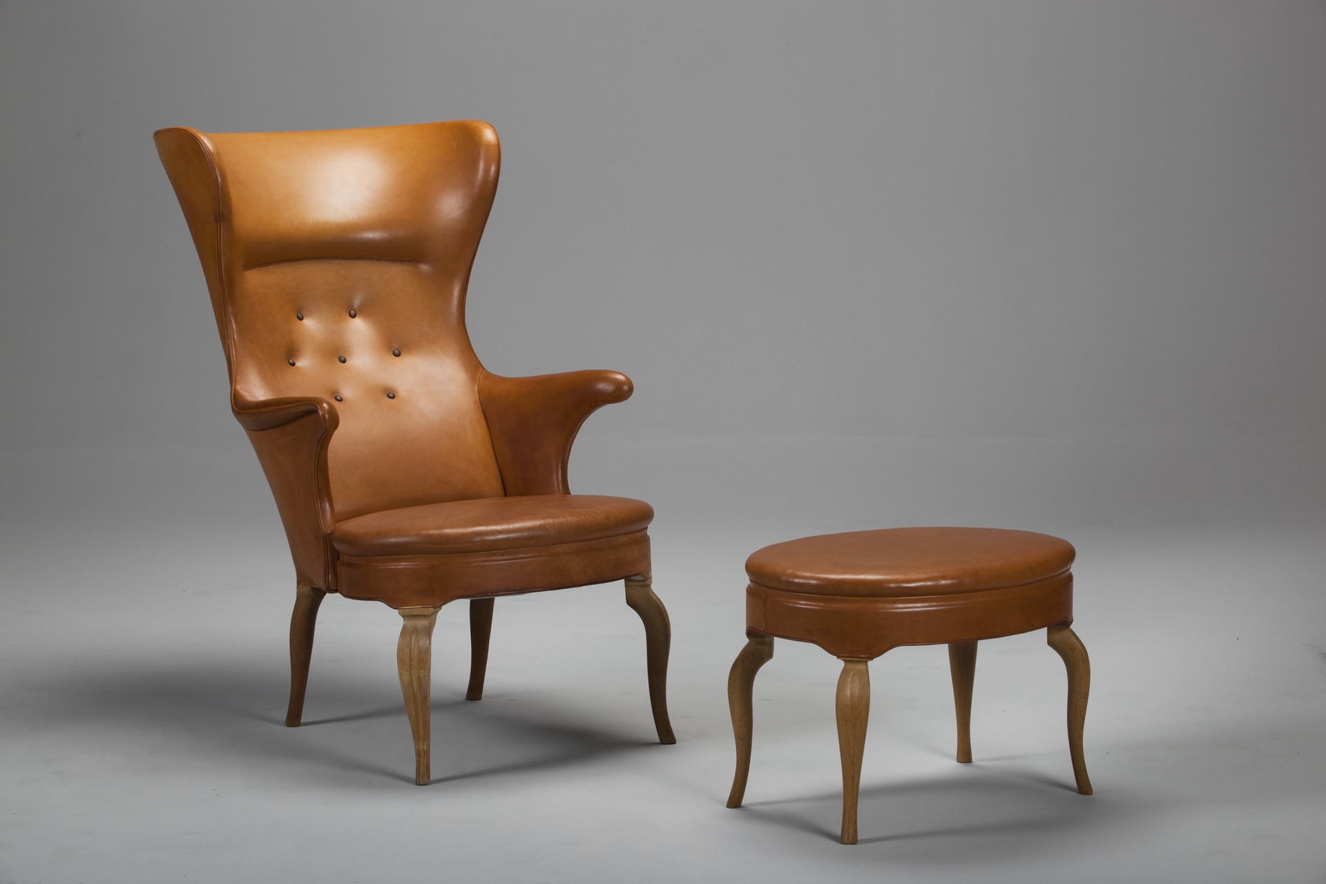 No.7972. Fritz Henningsen Wingback Chair and Footstool. Natural leather and oak legs, original buttons. Rare example with footstool.
Fritz Henningsen had been both a cabinet maker and retailer. Ca 1940.