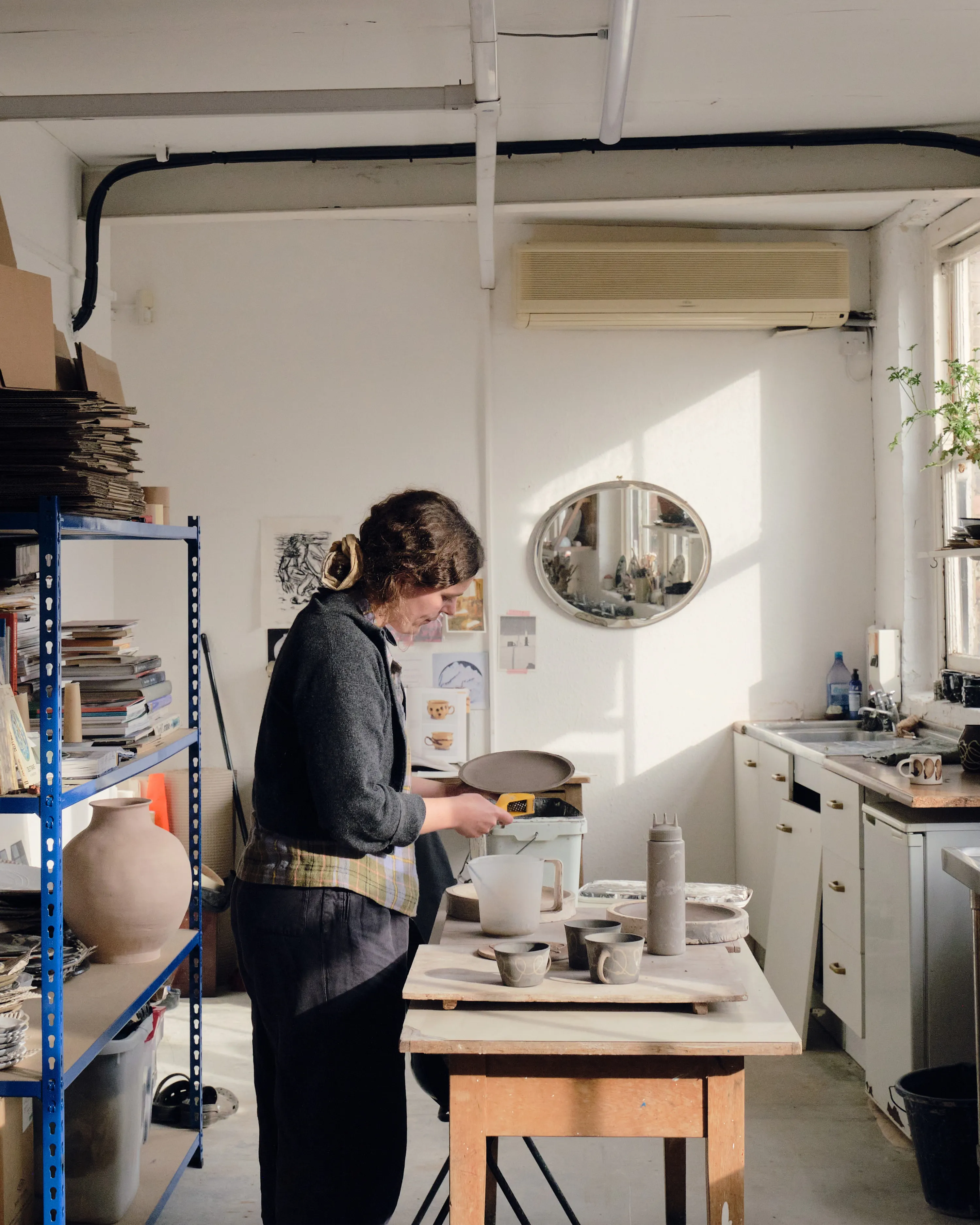 Green ware dries on the shelves behind Ali, before it is bisque fired